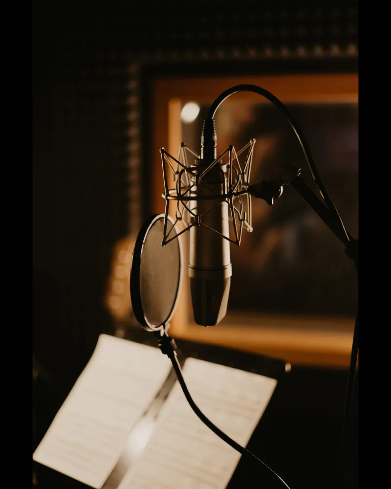Micrófono de estudio con filtro antipop montado en un soporte dentro de una cabina de voz en penumbra